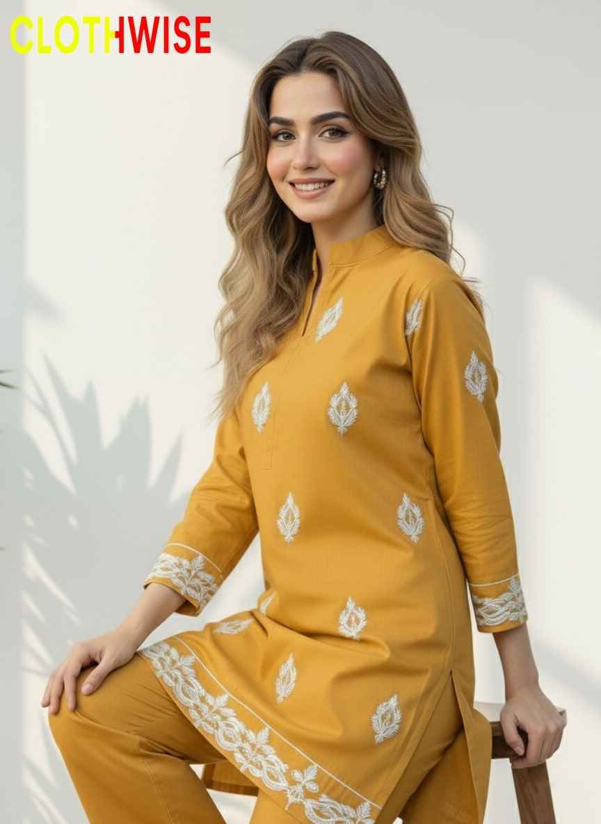 Woman wearing a mustard yellow traditional outfit with white patterns, sitting on a stool against a light background.
