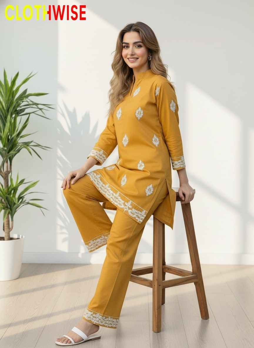 Woman in a mustard yellow outfit with white patterns sitting on a stool indoors.