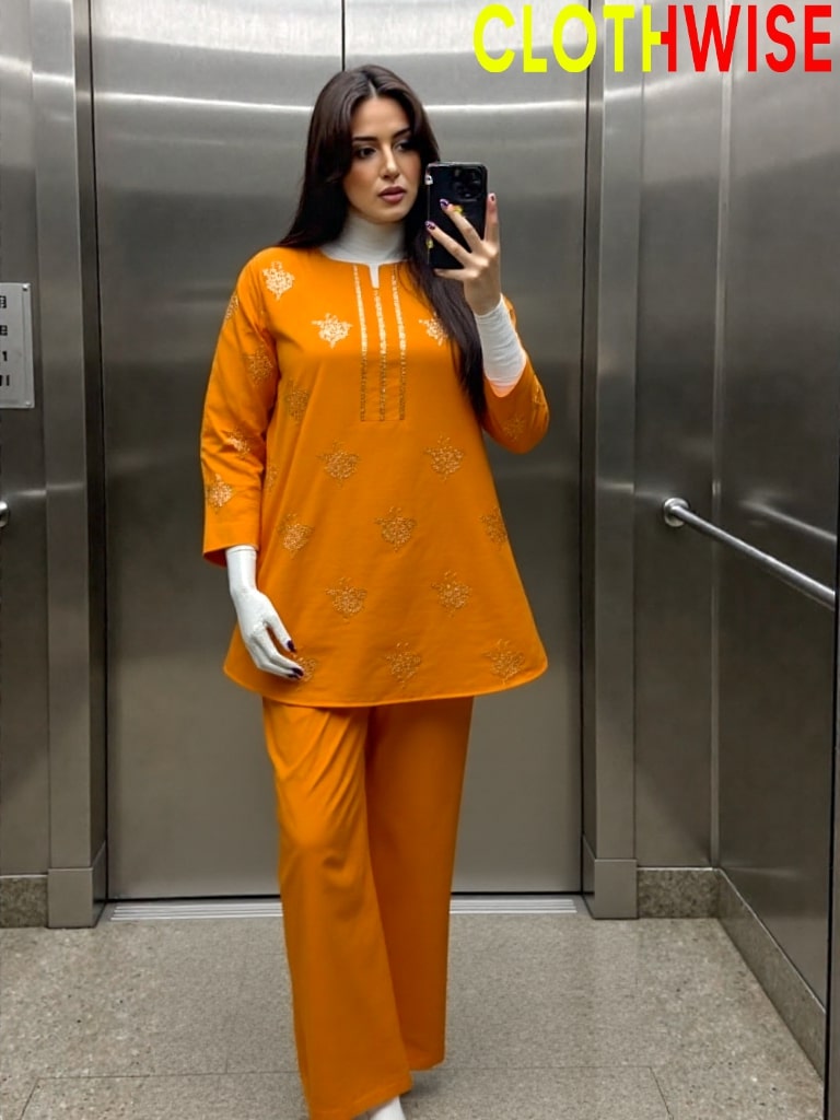 Woman taking a mirror selfie wearing an orange outfit in front of an elevator.