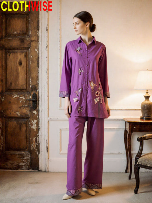 Woman wearing a purple outfit with embroidery in a room with a wooden door and lamp.