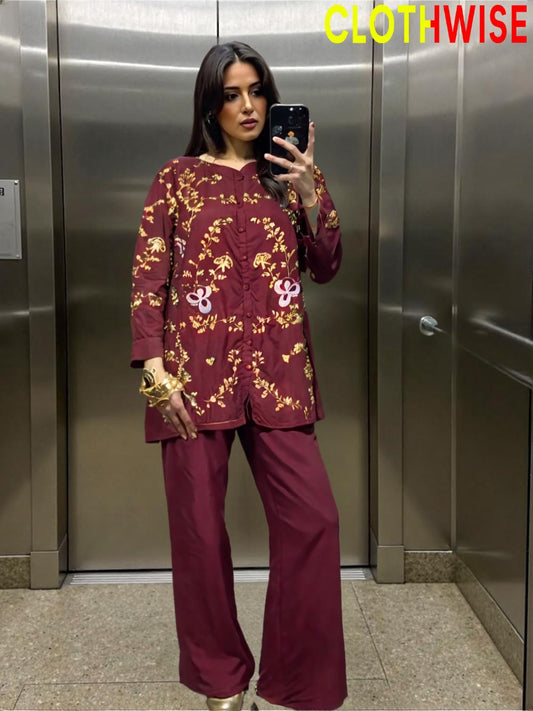 Woman taking a mirror selfie wearing a maroon outfit with gold patterns in an elevator.