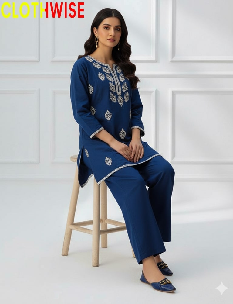 Woman wearing a blue embroidered outfit sitting on a stool against a white paneled wall with 'Clothwise' branding.