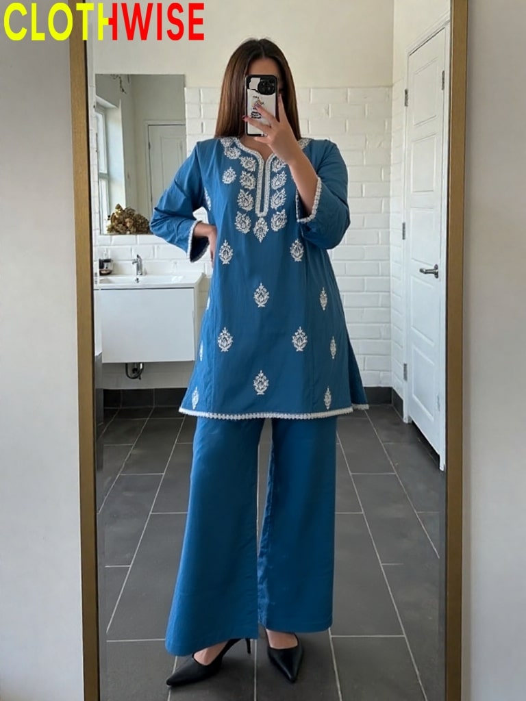 Woman taking a mirror selfie wearing a blue embroidered outfit in a bathroom.