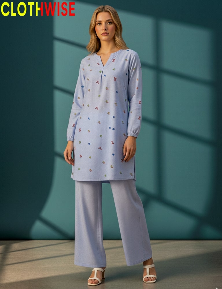 Woman wearing a light blue outfit with a pattern, standing against a teal wall.