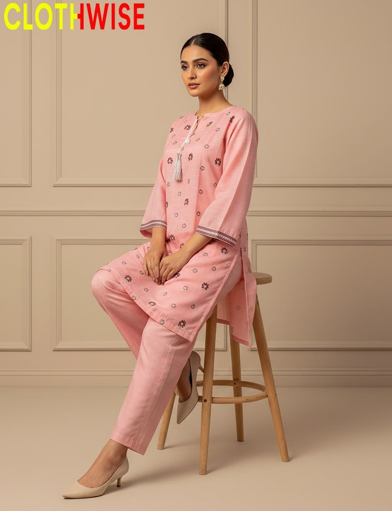 Woman wearing a pink outfit with floral patterns sitting on a stool against a beige wall, with 'CLOTHWISE' branding.