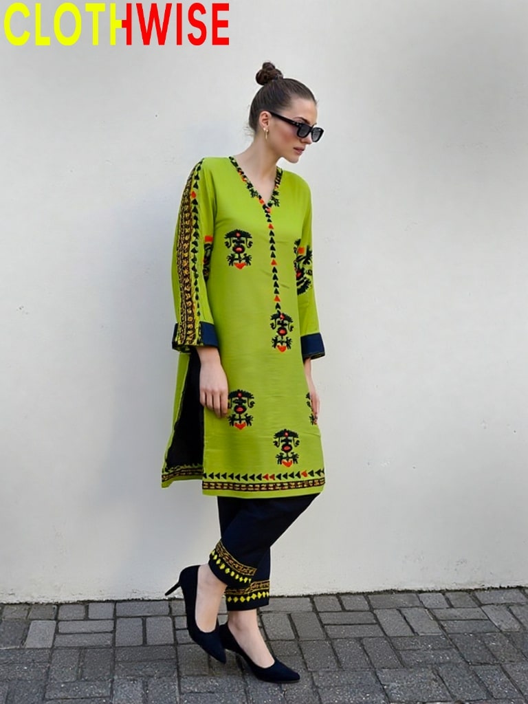 Woman wearing a green embroidered dress with black pants against a white wall, branded 'CLOTHWISE'.