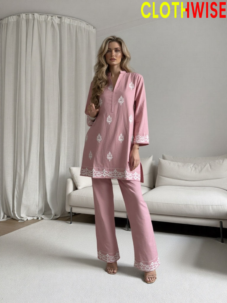 Woman wearing a pink outfit with white embroidery in a minimalistic room.