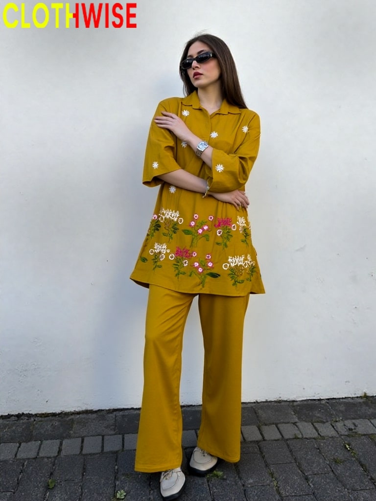 Woman wearing a mustard yellow outfit with floral embroidery against a white wall, branded 'CLOTHWISE'.