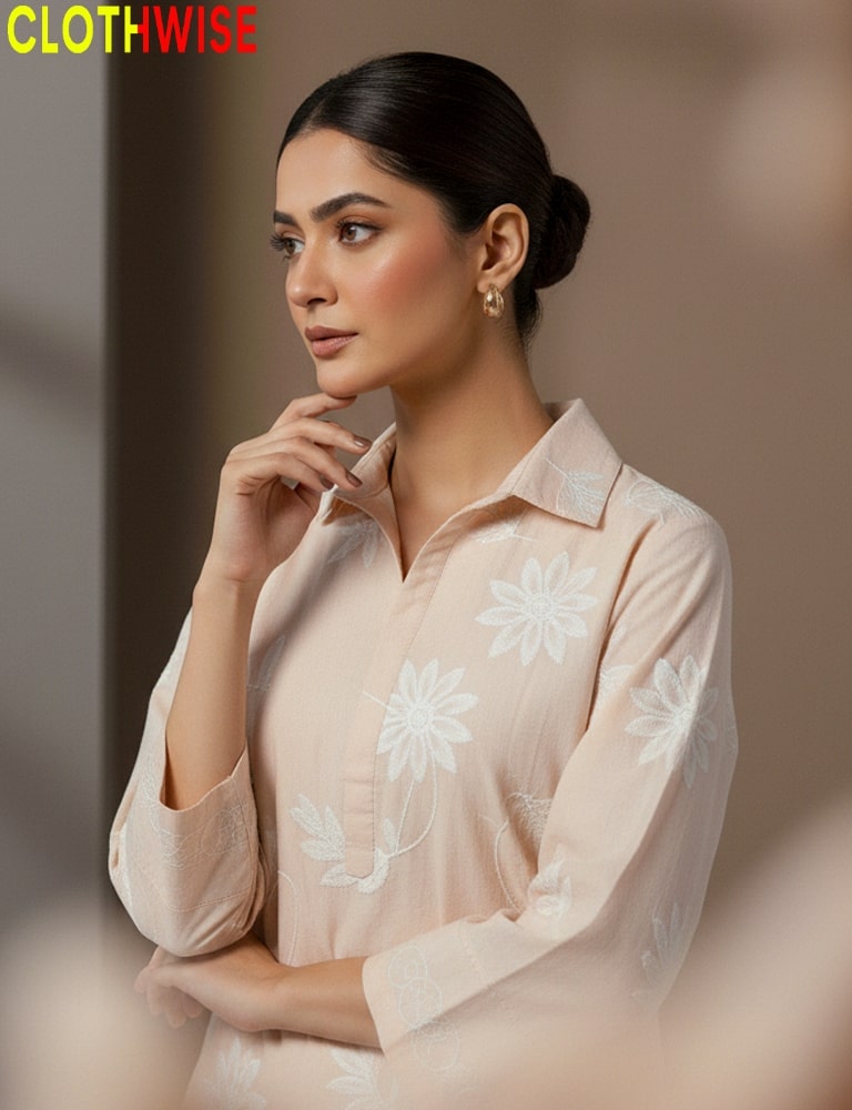 Woman wearing a light pink shirt with floral embroidery, sitting against a blurred background with 'CLOTHWISE' branding.