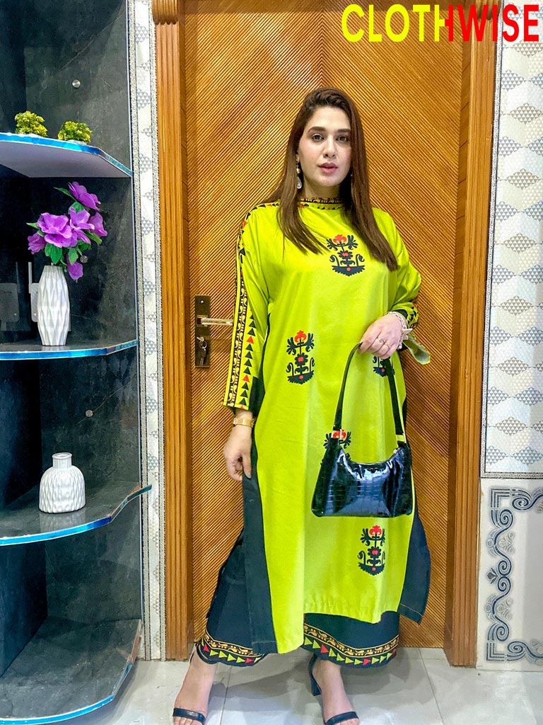 Woman in a bright green traditional outfit with floral patterns standing indoors.