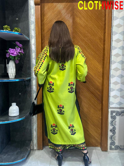 Person wearing a bright green embroidered dress standing in front of a wooden door.