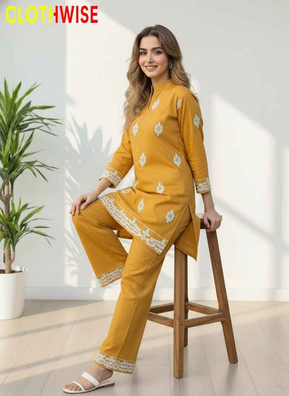 Woman in a mustard yellow outfit with white patterns sitting on a stool indoors.