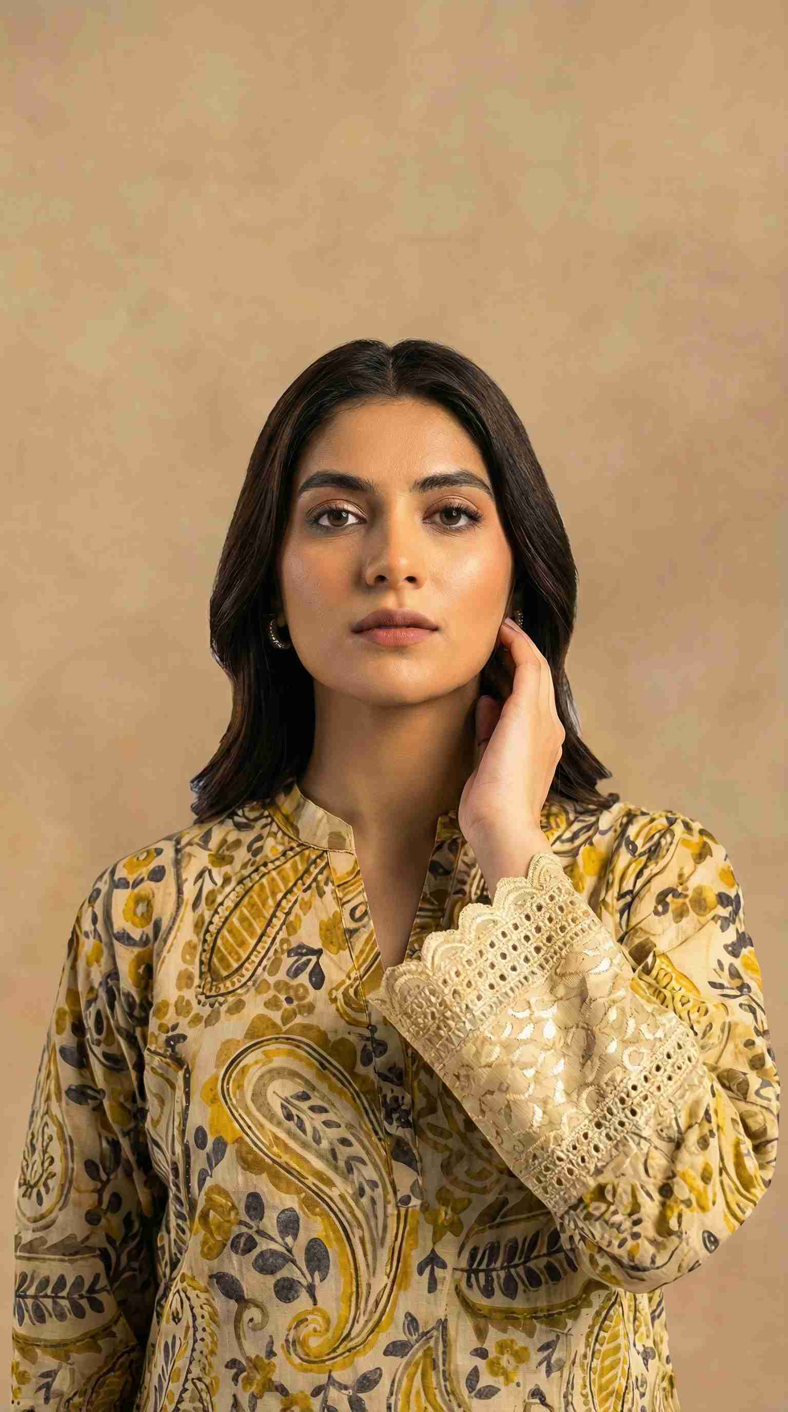 Woman wearing a patterned yellow and black outfit with lace sleeves against a beige background
