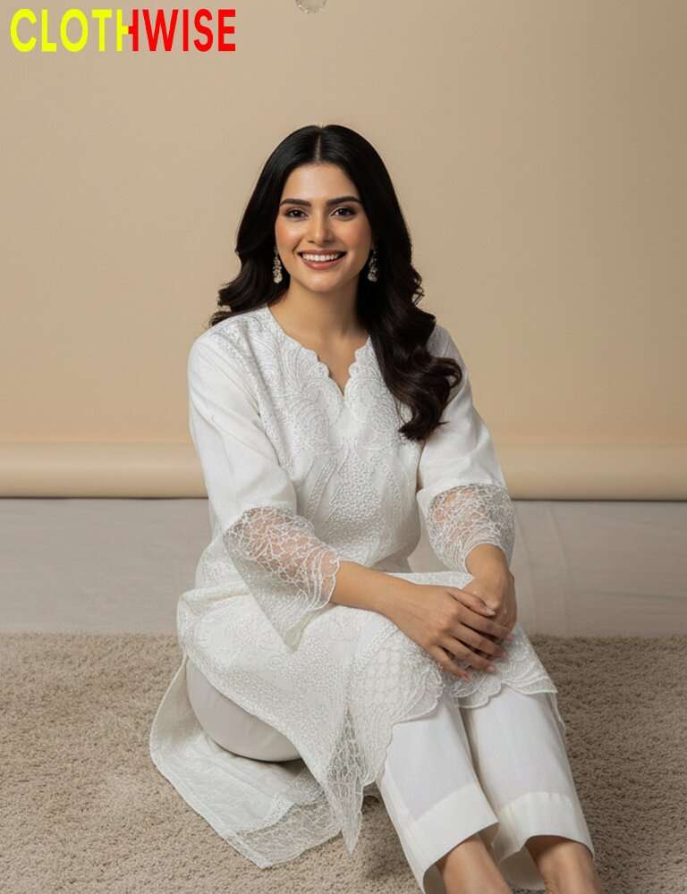 Woman wearing a white outfit with lace details, sitting on the floor against a beige wall.