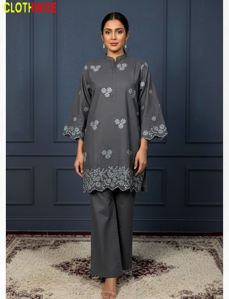 Woman wearing a gray embroidered outfit against a dark blue paneled wall.