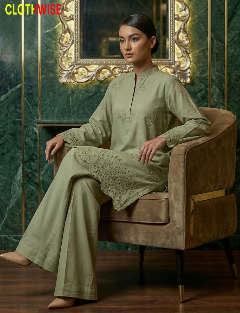 Woman in a green outfit sitting on a brown chair with a decorative mirror in the background.