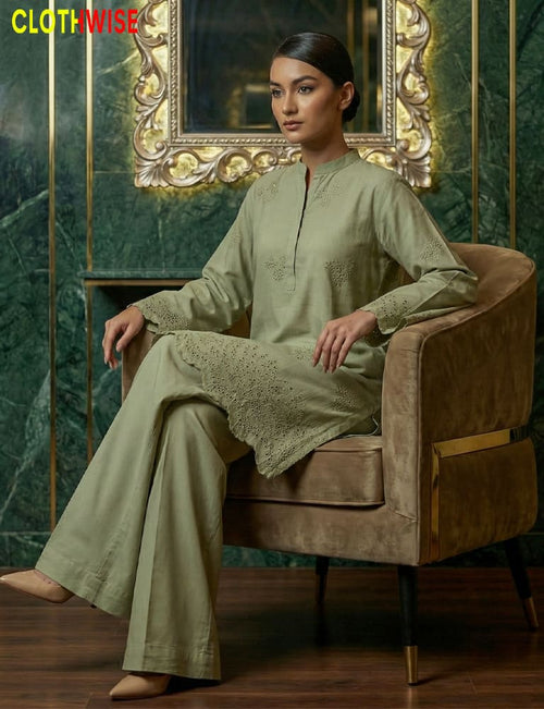 Woman in a green outfit sitting on a brown chair with a decorative mirror in the background.