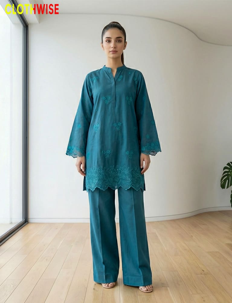 Woman wearing a teal outfit with lace details in a minimalistic room.