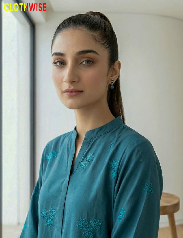 Woman wearing a teal embroidered shirt with a blurred indoor background