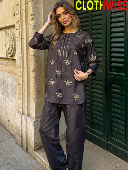 Woman wearing a dark outfit with floral patterns standing against a building.