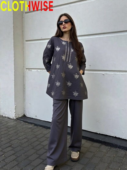 Woman wearing a dark gray outfit with floral patterns against a white wall.