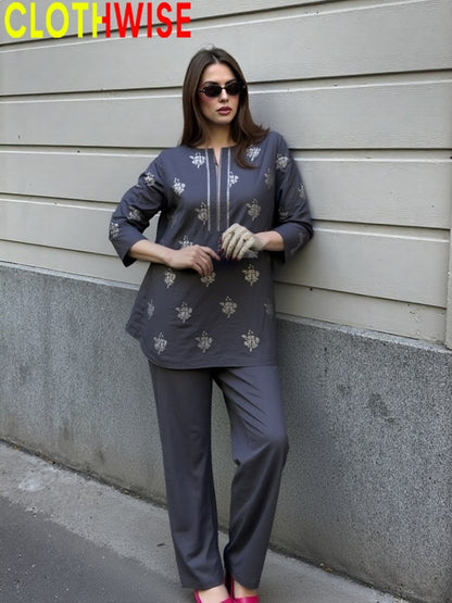 Woman wearing a gray outfit with floral patterns against a gray wall.