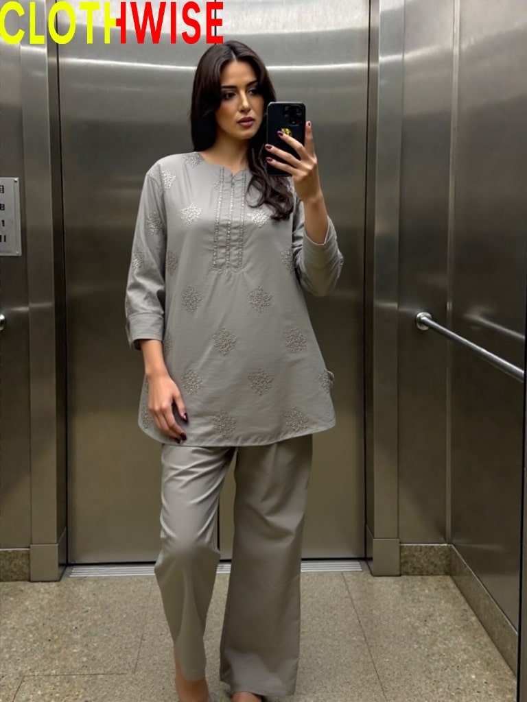 Woman taking a mirror selfie wearing a gray outfit in an elevator.