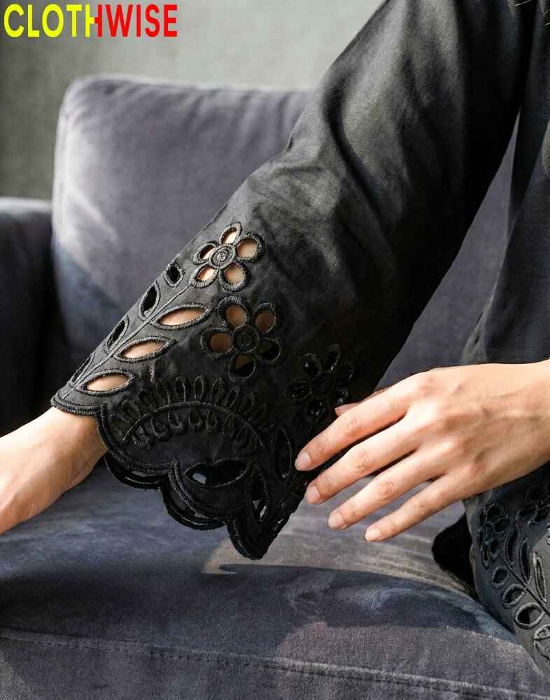 Person wearing black lace-up shoes with floral designs, sitting on a gray couch.