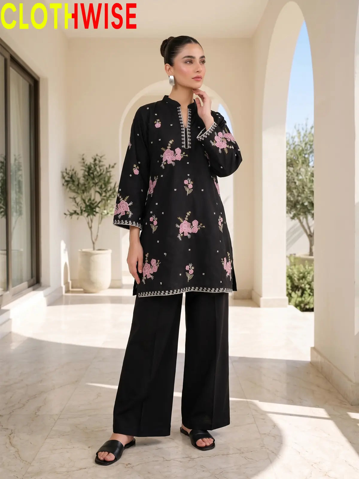 Front view of a model wearing a black embroidered straight tunic and matching palazzo pants against an outdoor arches backdrop