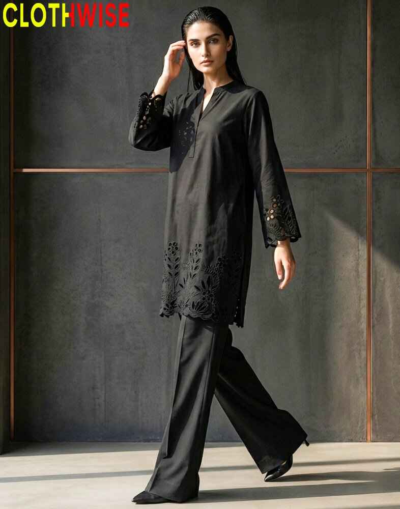 Woman wearing a black outfit with embroidery, standing against a dark background.