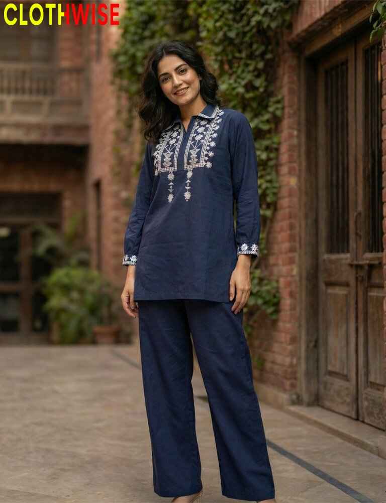 Woman wearing a navy blue embroidered outfit standing in front of a brick wall.