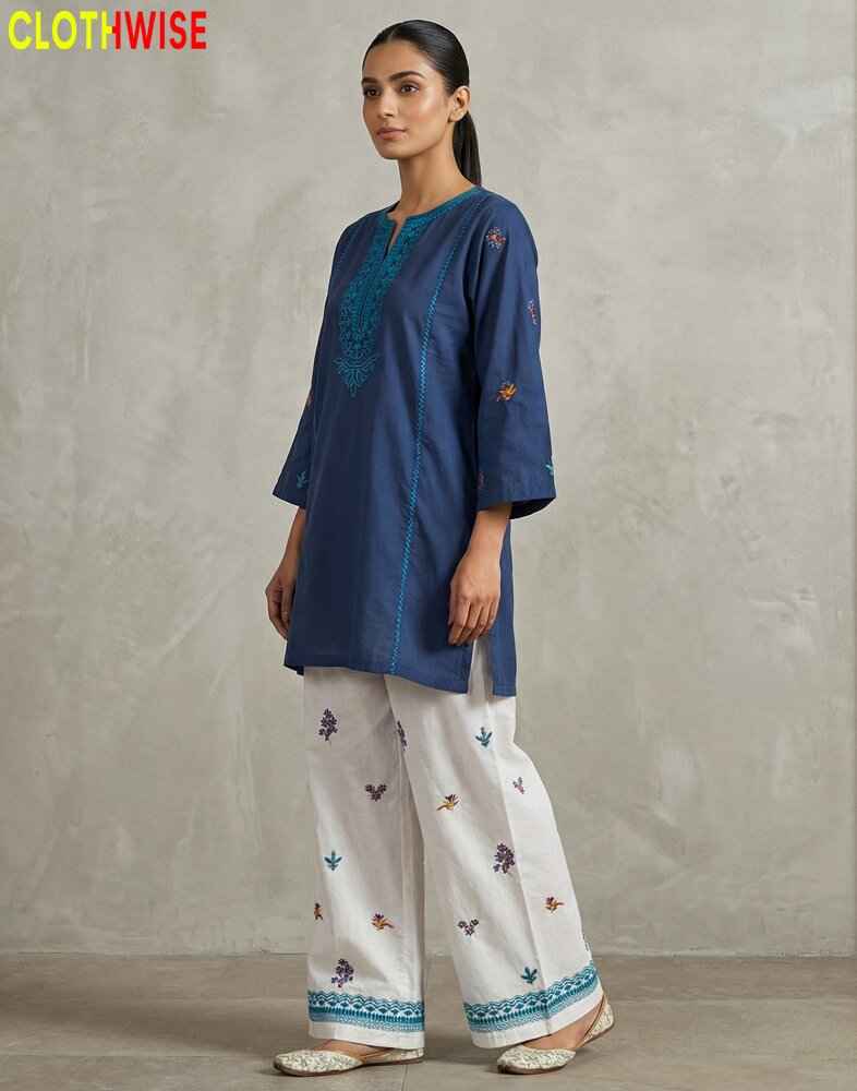 Woman wearing a blue top and white pants with embroidery, standing against a plain background. Brand 'CLOTHWISE' visible.