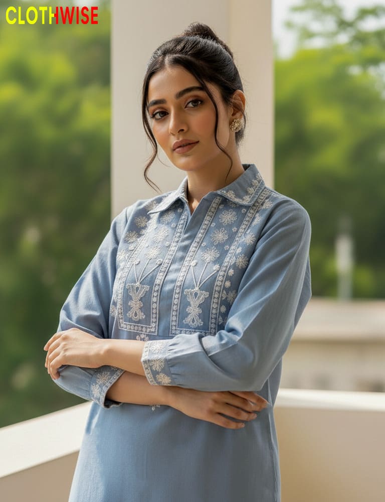 Woman wearing a light blue embroidered shirt with a blurred green outdoor background