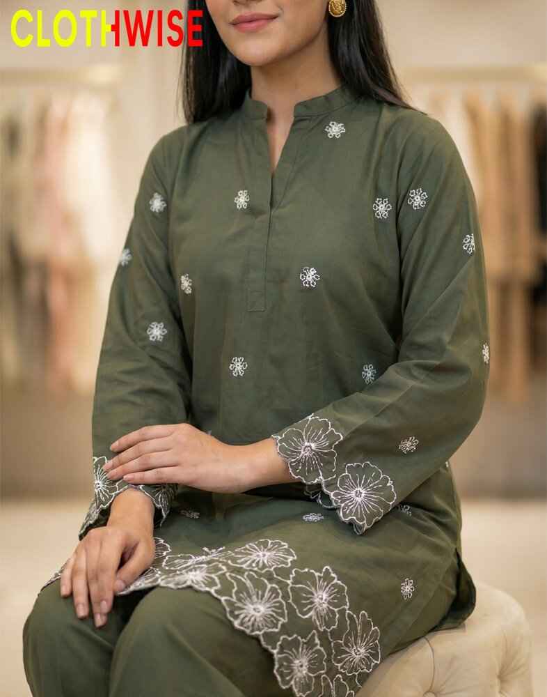 Woman wearing a green kurta with white floral embroidery, sitting on a beige chair.