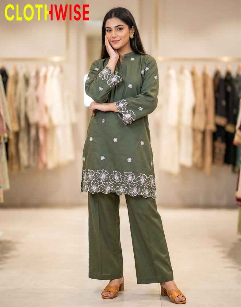 Woman wearing a green outfit with white embroidery in a clothing store.