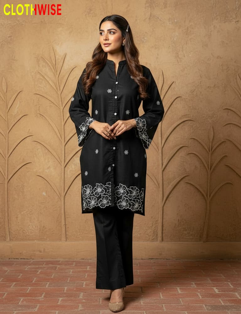 Woman wearing a black outfit with floral patterns against a beige wall.