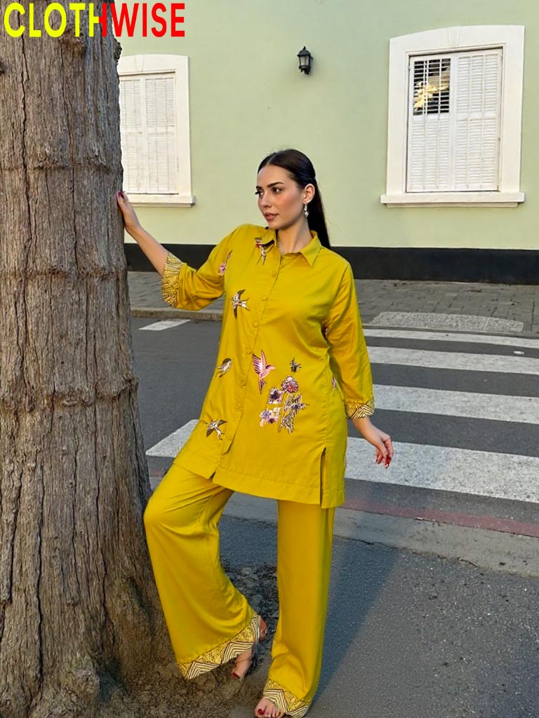 Woman in a yellow outfit standing next to a tree on a street.