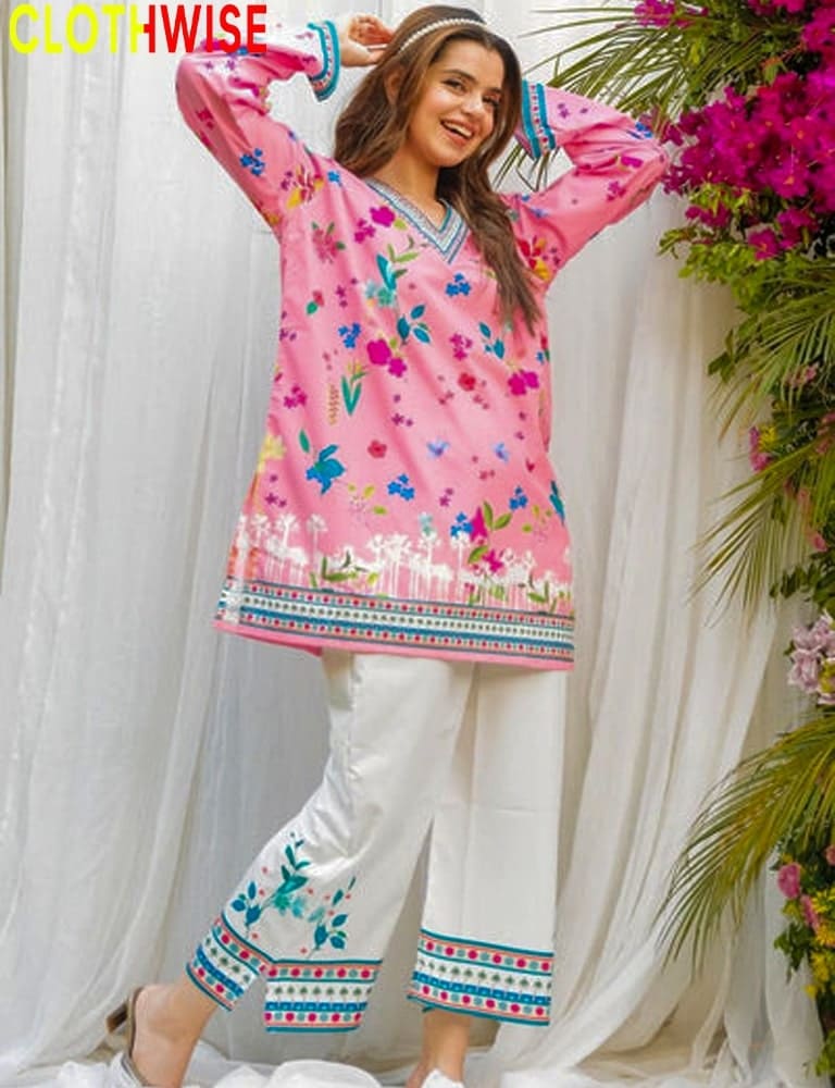 Woman wearing a pink floral top and white pants with embroide, standing against a white curtain with floral decorations.