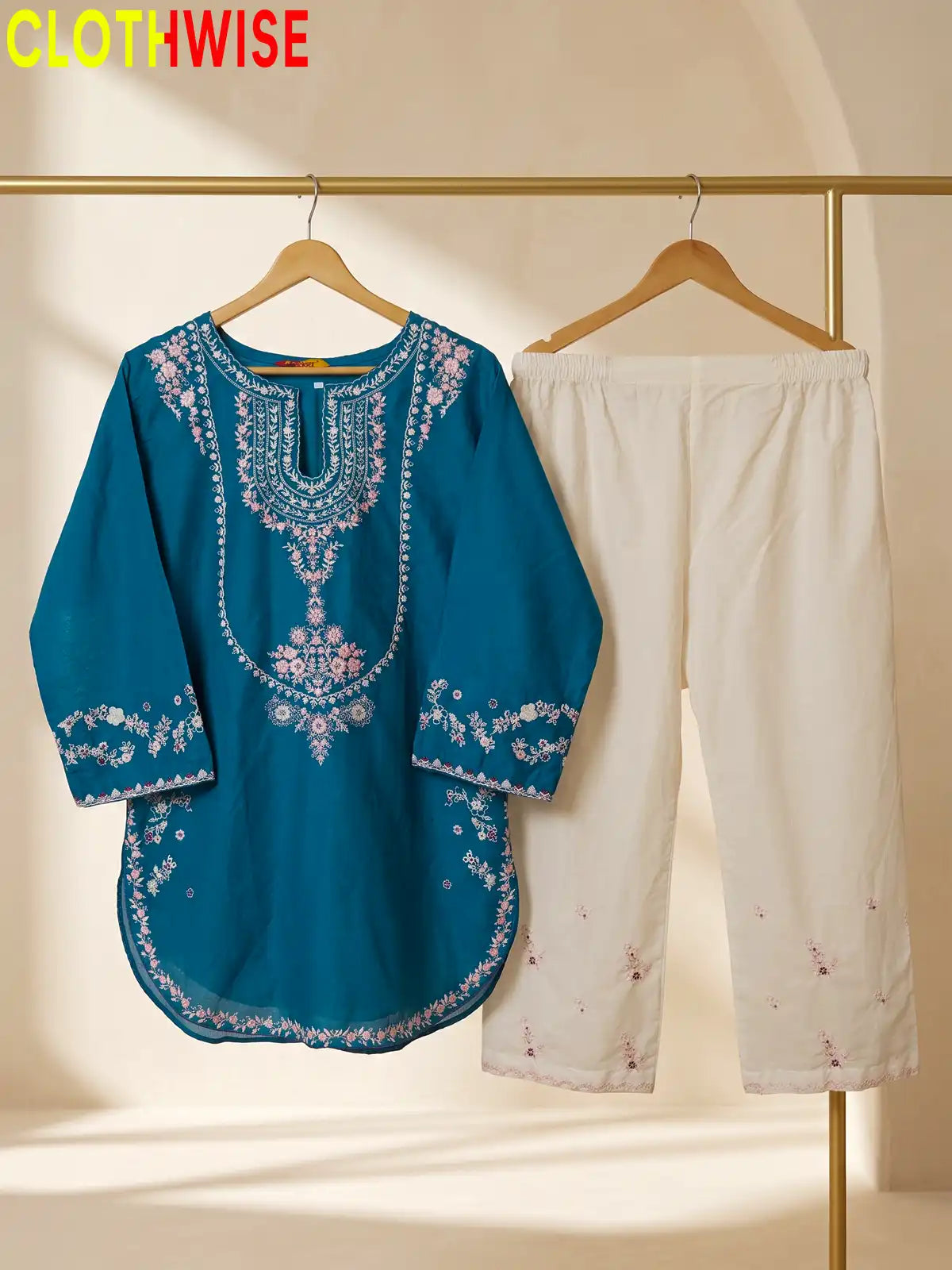 A teal blue embroidered kurta with white floral embroidery hanging next to white cropped pants on a clothing rack, with the CLOTHWISE logo in the top left corner.