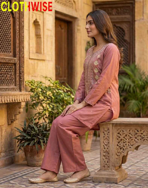 Woman in traditional outfit sitting on a stone bench with ornate carvings, against a warm-toned architectural background.