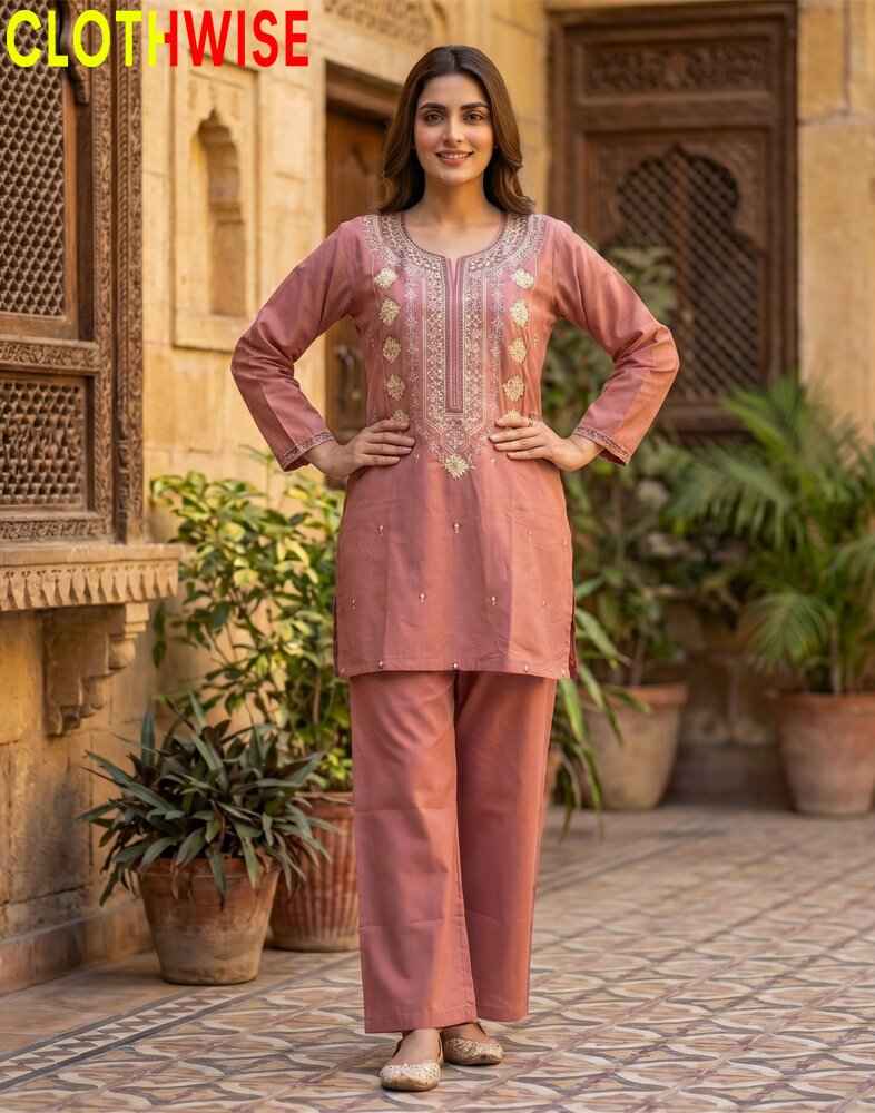 Woman in a peach traditional outfit standing in front of a decorative wall with plants.