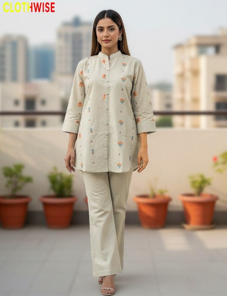 Woman wearing a beige outfit with floral patterns on a rooftop with plants and buildings in the background.