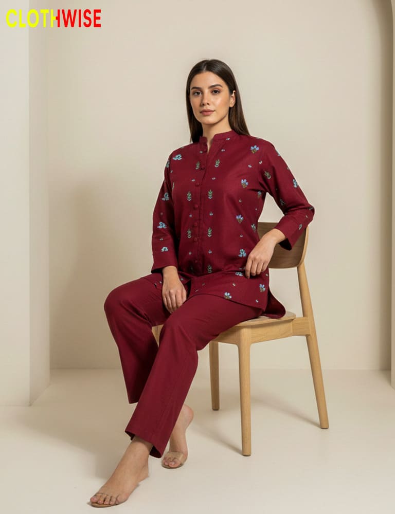 Woman wearing a maroon pajama set with floral patterns, sitting on a chair against a beige background. Brand 'Clothwise' visible.