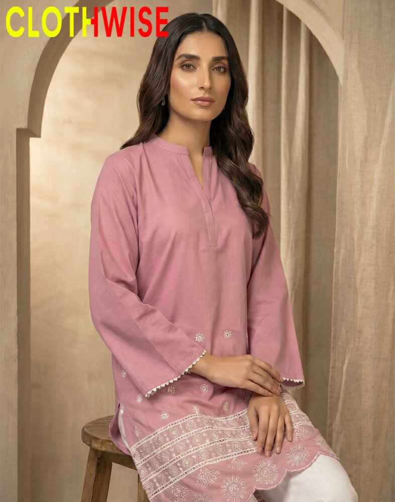 Woman wearing a pink kurta with white embroidery sitting on a wooden stool against a beige wall.
