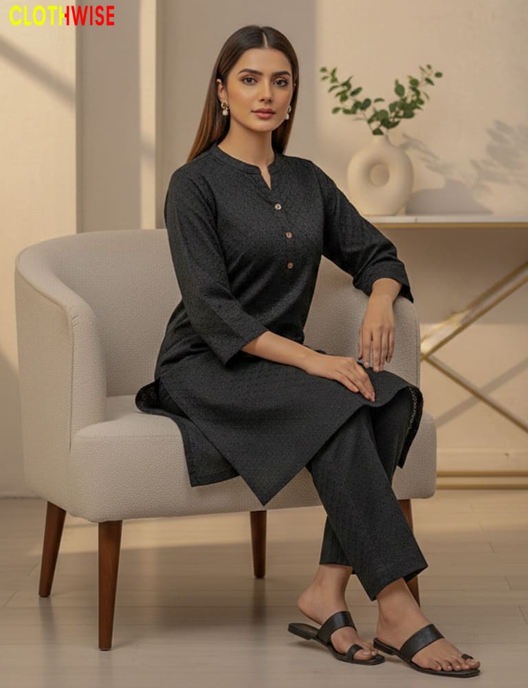 Woman sitting on a chair wearing a dark gray kurta with pants in a minimalistic room.