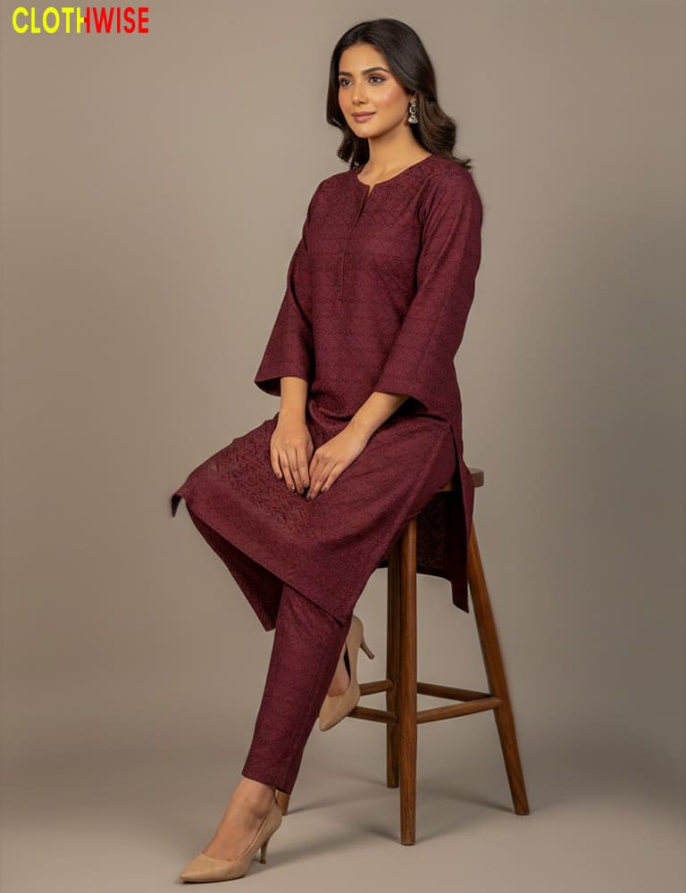 Woman wearing a maroon outfit sitting on a wooden stool against a plain background