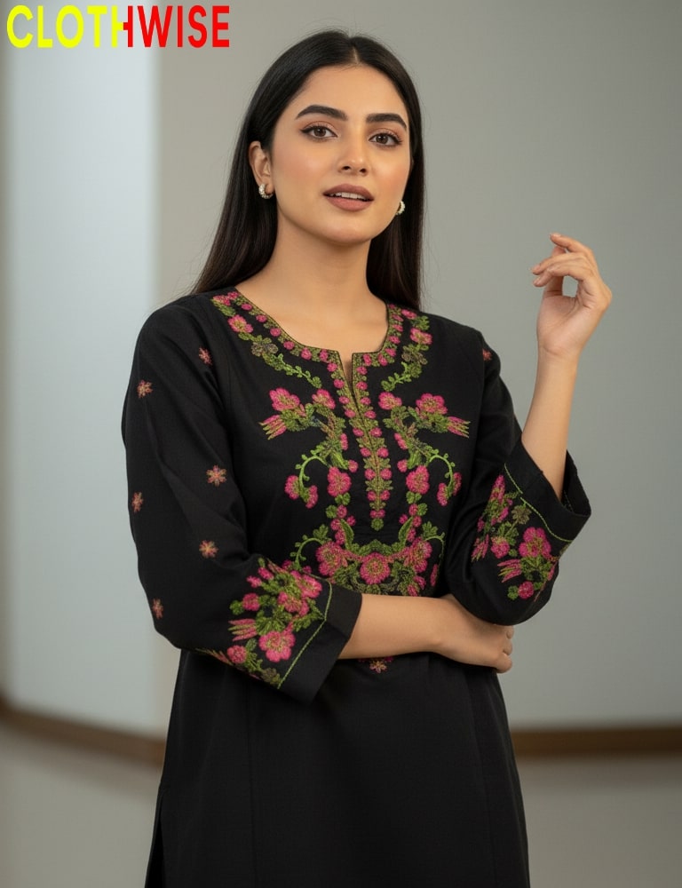 Woman wearing a black embroidered top with pink and green details, standing against a neutral background.