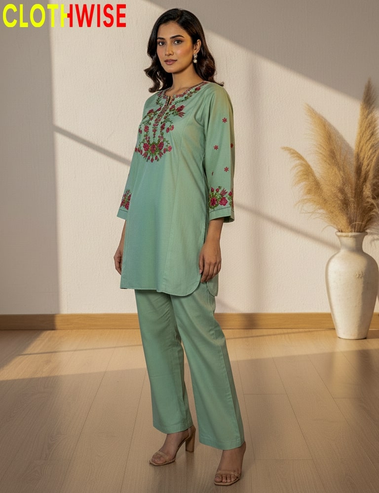 Woman wearing a light green outfit with floral embroidery in a minimalistic setting.
