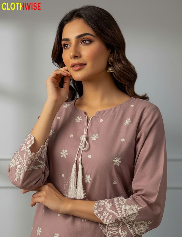 Woman wearing a mauve top with white floral embroidery, posing against a plain background.