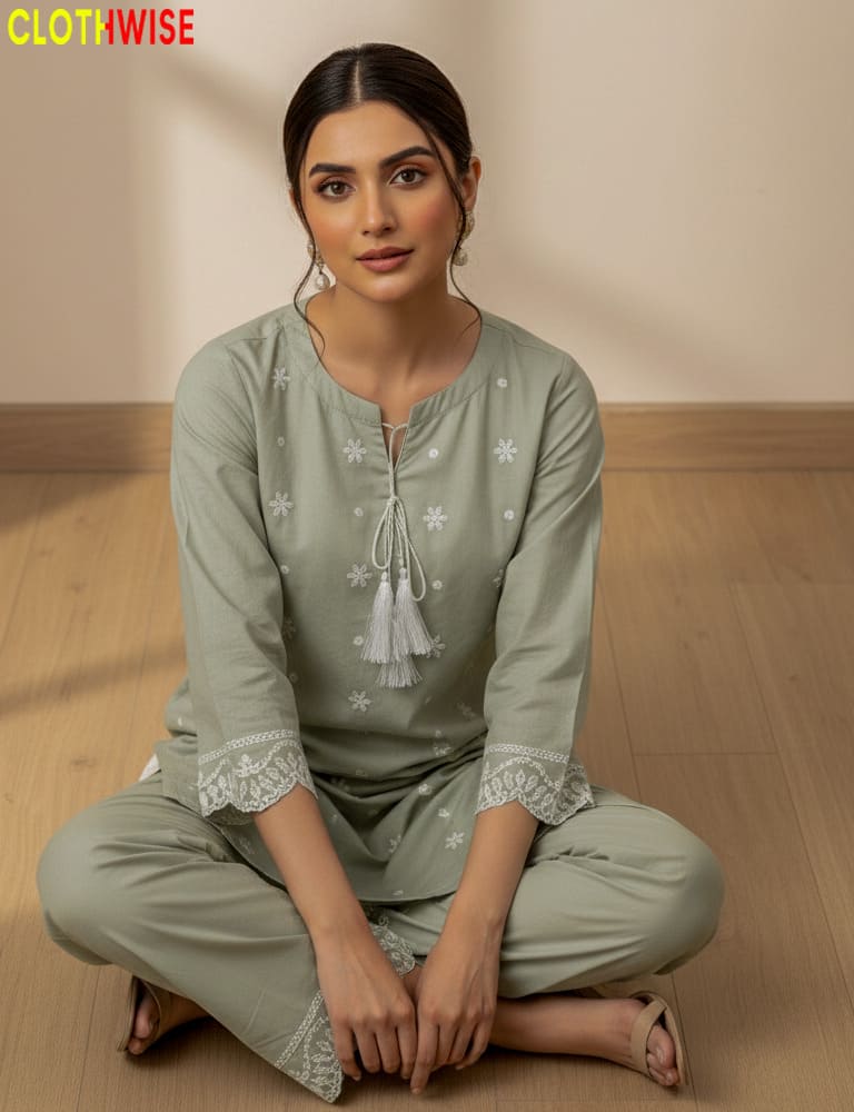 Woman wearing aoatmeal  traditional outfit with intricate designs, sitting on a wooden floor.